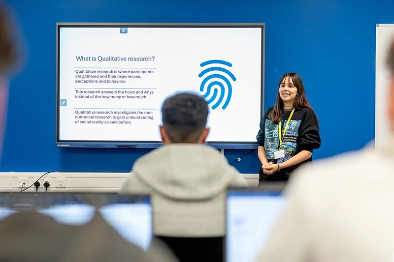 Students watching a lecturer present next to projection screen