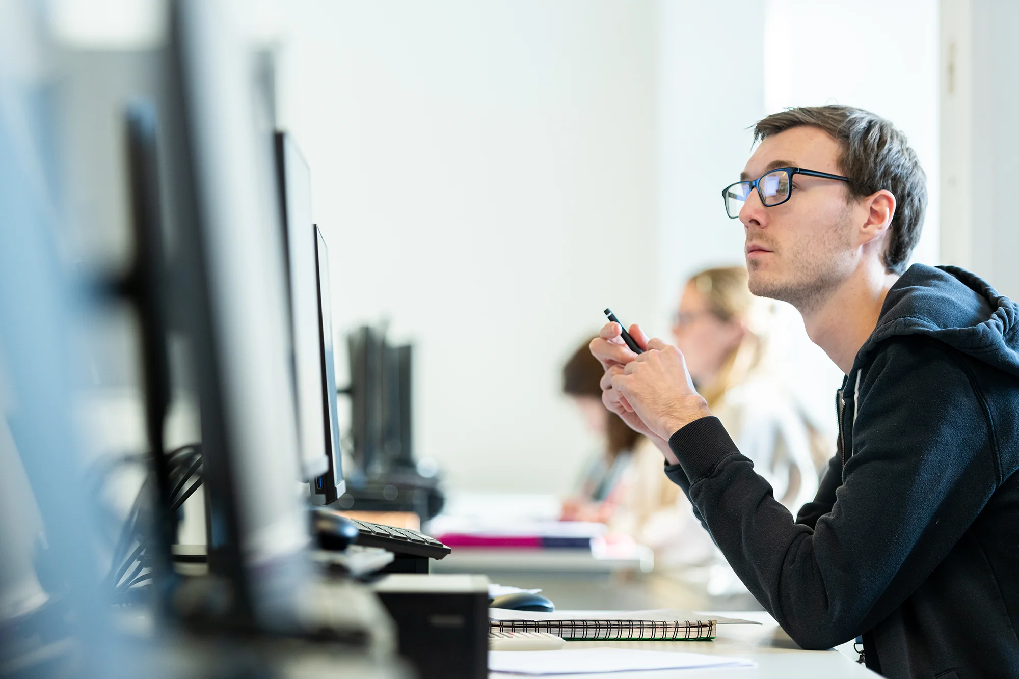 Young man holding a pen looking at a computer monitor