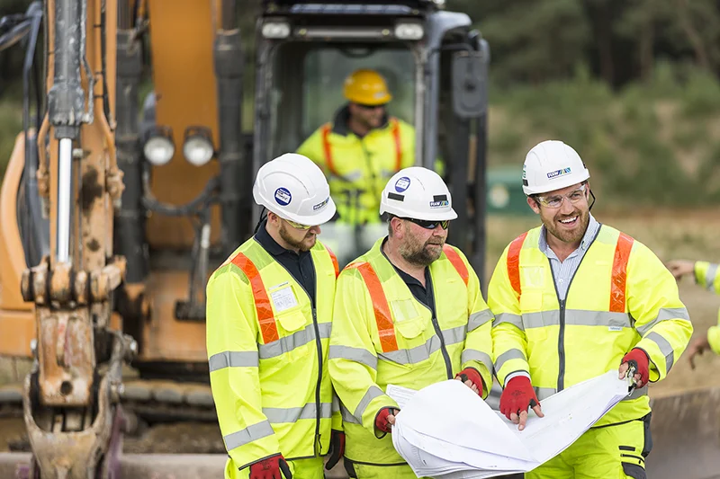 Three workers in in protective equipment on a building site looking at plans