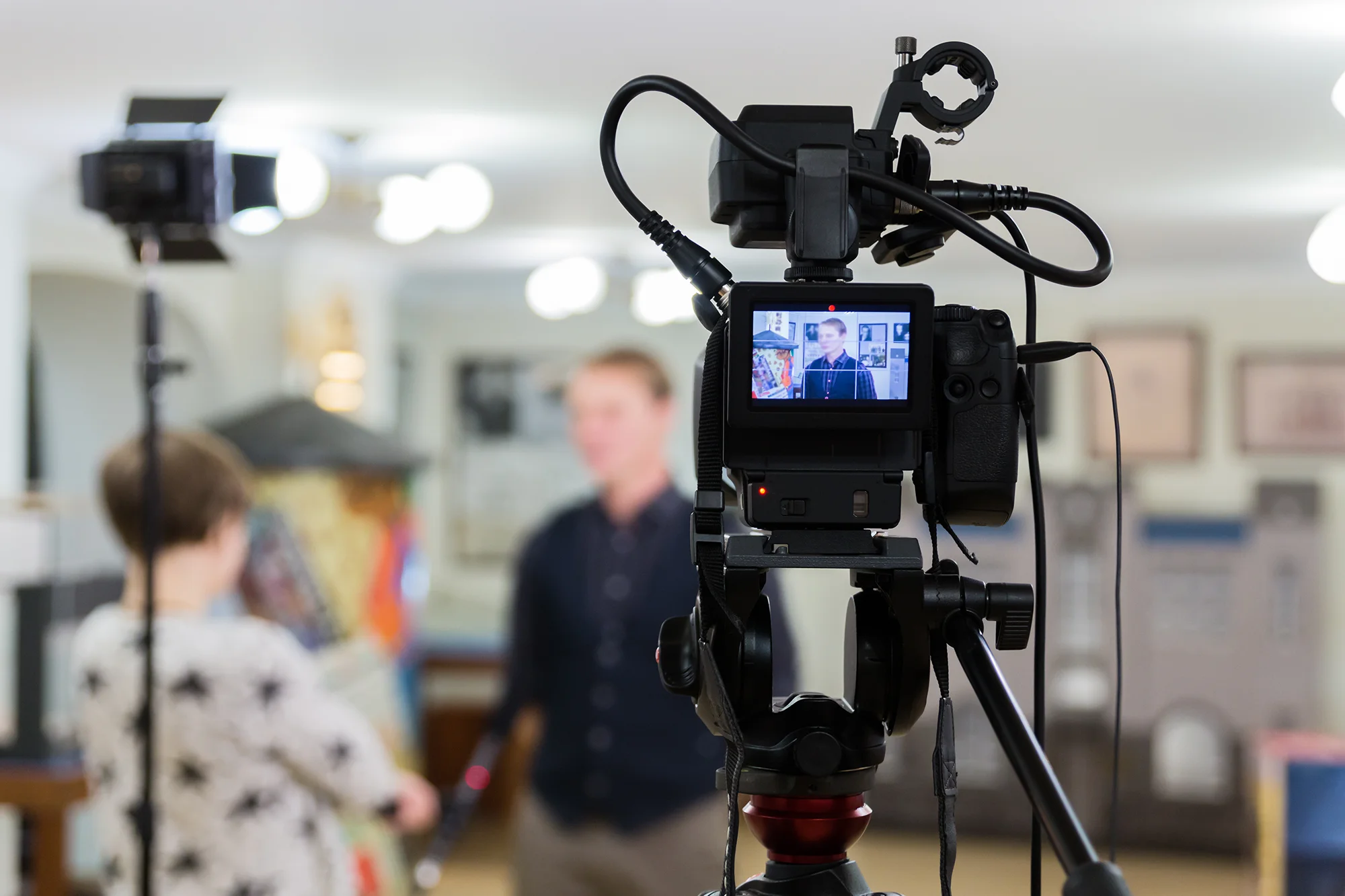 A black video camera on a tripod filming two people